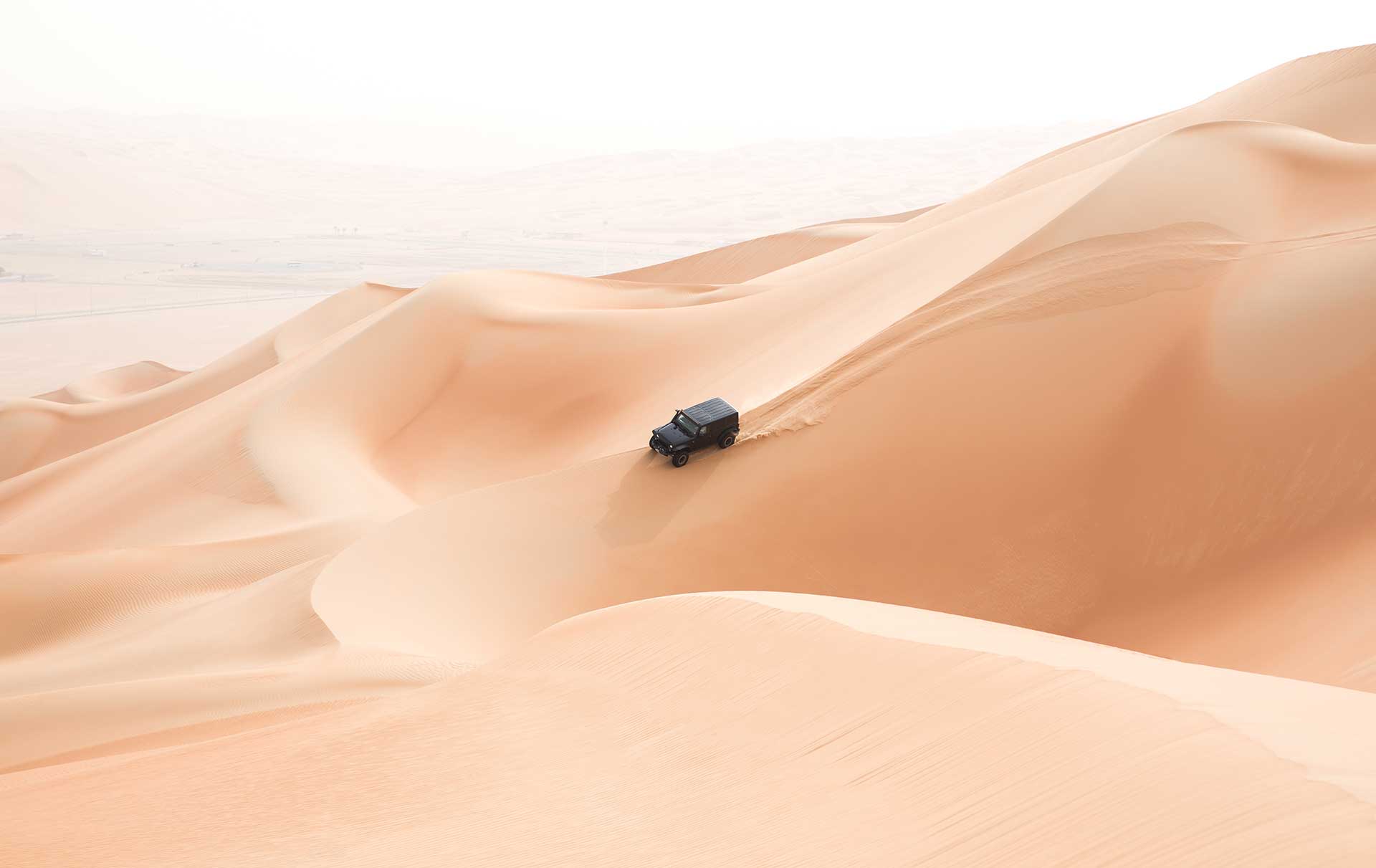 A single black car scaling giant sand dunes in the Empty Quarter desert