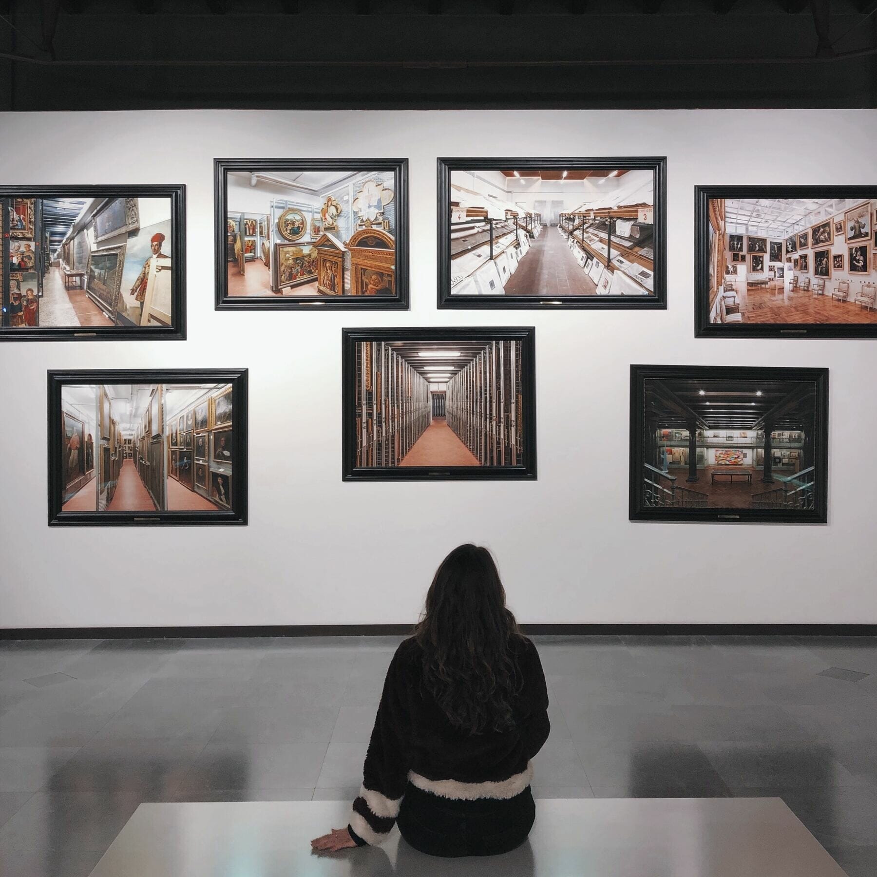 Woman seated with her back turned looking at seven pictures on a wall