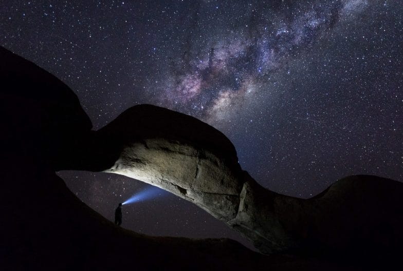 Person under a rock arch with milky way above